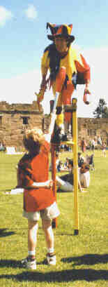 A young lad hands a club up to Kris Katchit the stiltwalking jester